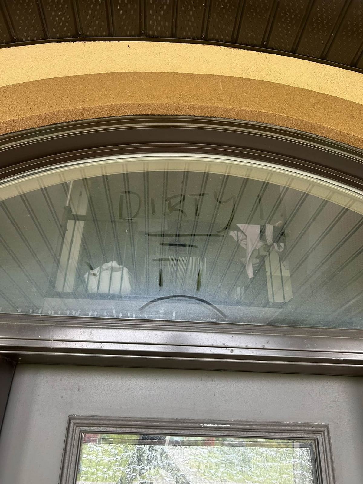 Dusty arched window with the word dirty written in the dust