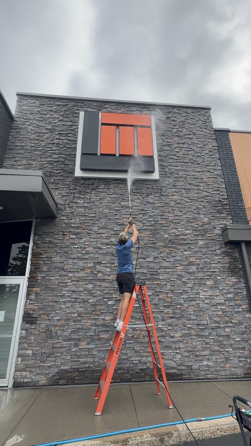 Crew member on a ladder pressure washing a commercial sign